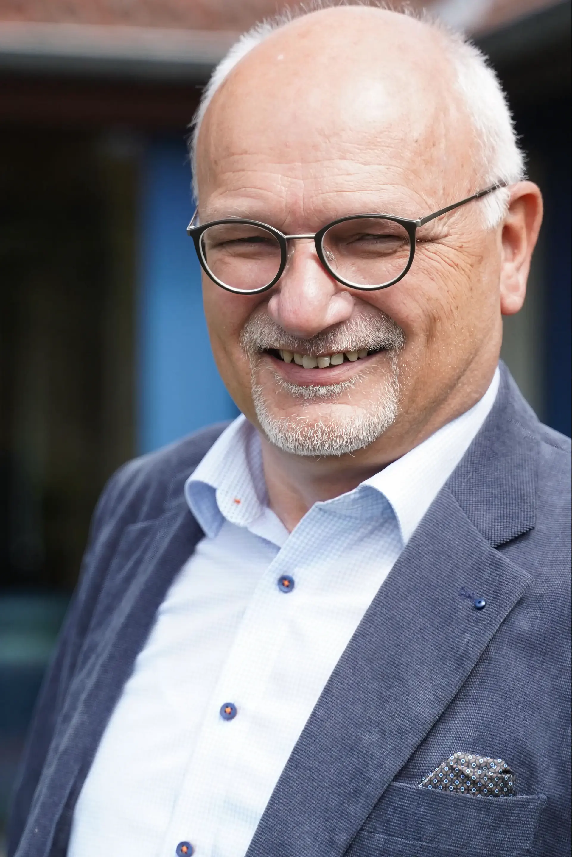 Eckhard Lueling, ein Mann mit Brille und grauem Bart, lächelt in einem blauen Anzug.